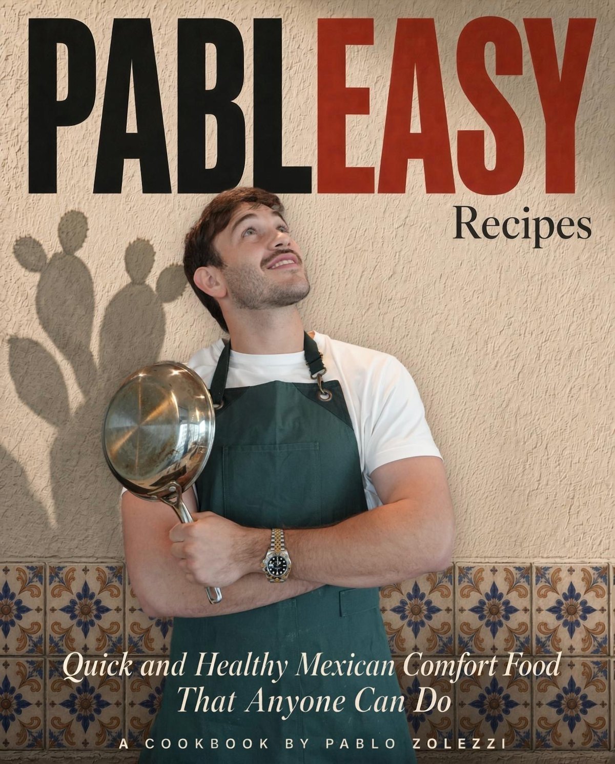 Pableasy Recipes cover: Pablo in a green apron holding a pan against a stucco wall with Talavera tile